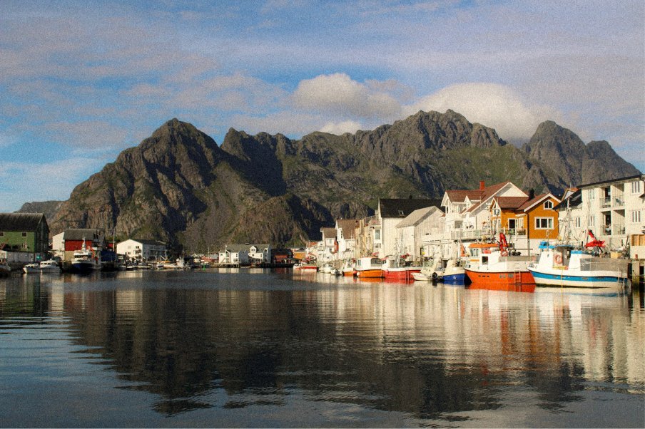Henningsvær harbour with colourful houses and boats reflected in calm water beneath Lofoten peaks