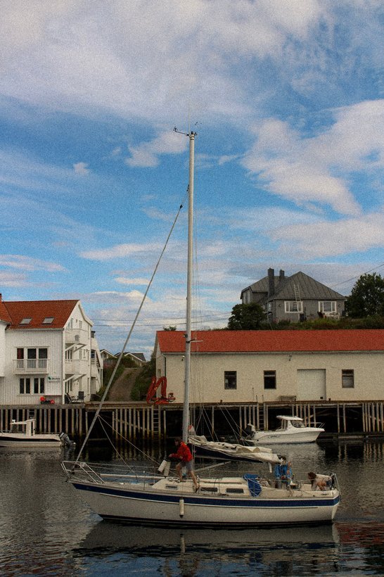 Sailing boat moored by red and white buildings under a blue sky in Lofoten