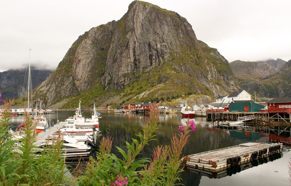 Steep mountain rising above the harbour and red rorbuer at Hamnøy, Lofoten