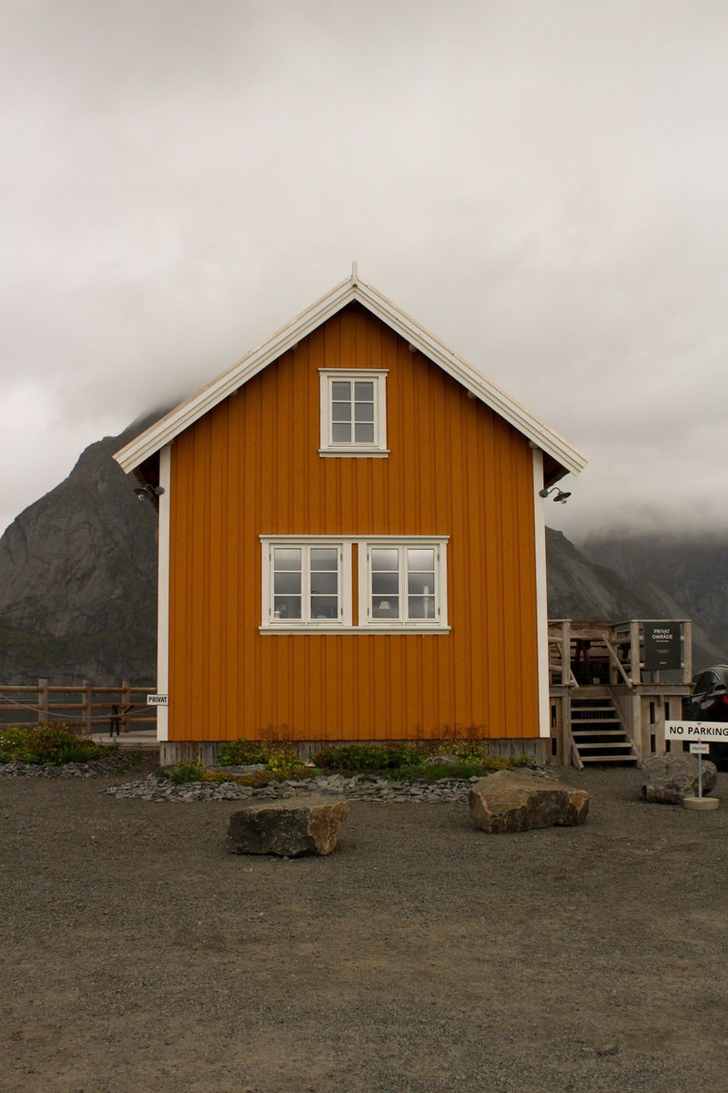 Yellow house beneath a misty mountain in Sakrisøy, Lofoten