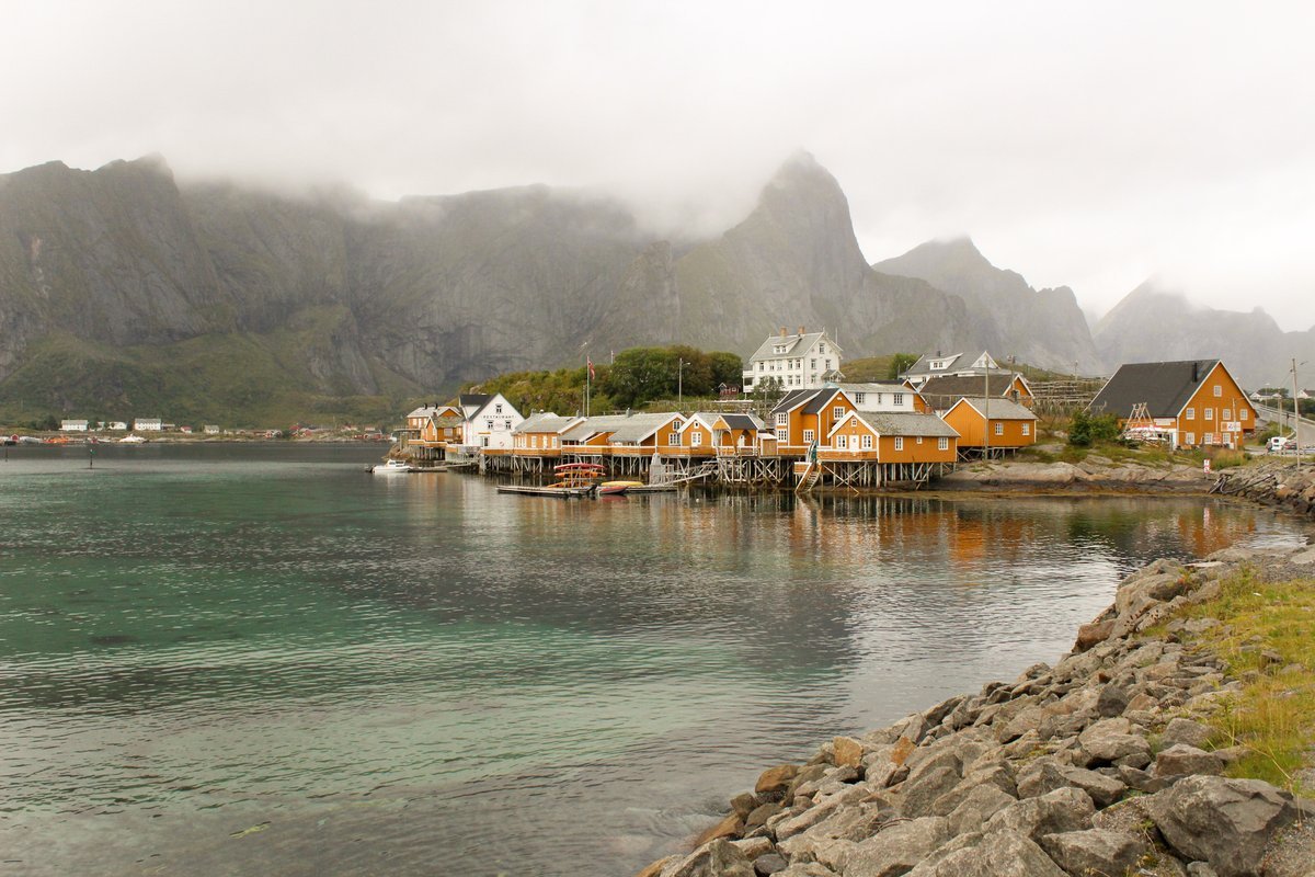 Yellow rorbuer of Sakrisøy by the sea with mountains in the mist, Lofoten