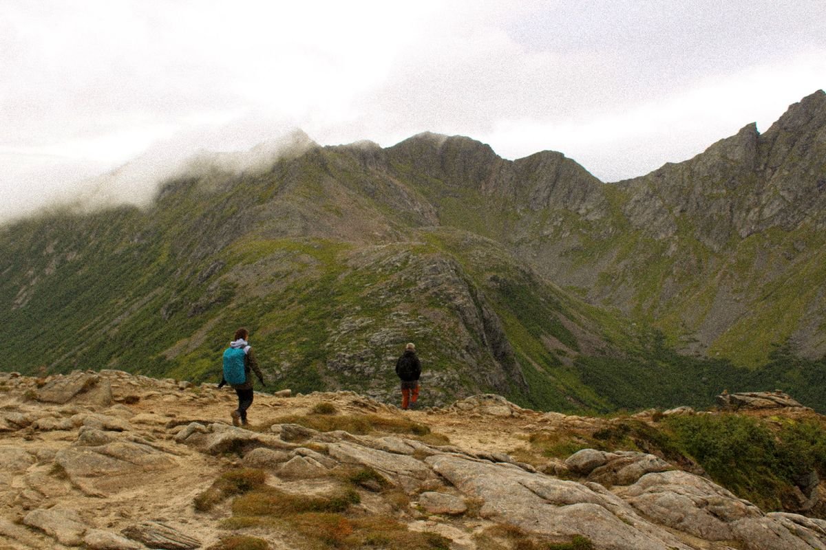 Hikers climbing a rocky trail among green mountains in Lofoten