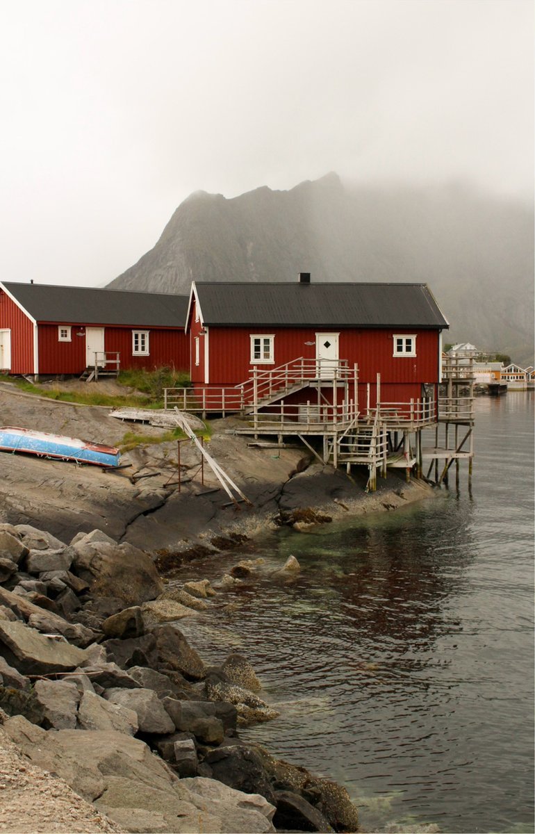 Red rorbuer on stilts by the rocky shore under a misty mountain in Hamnøy, Lofoten