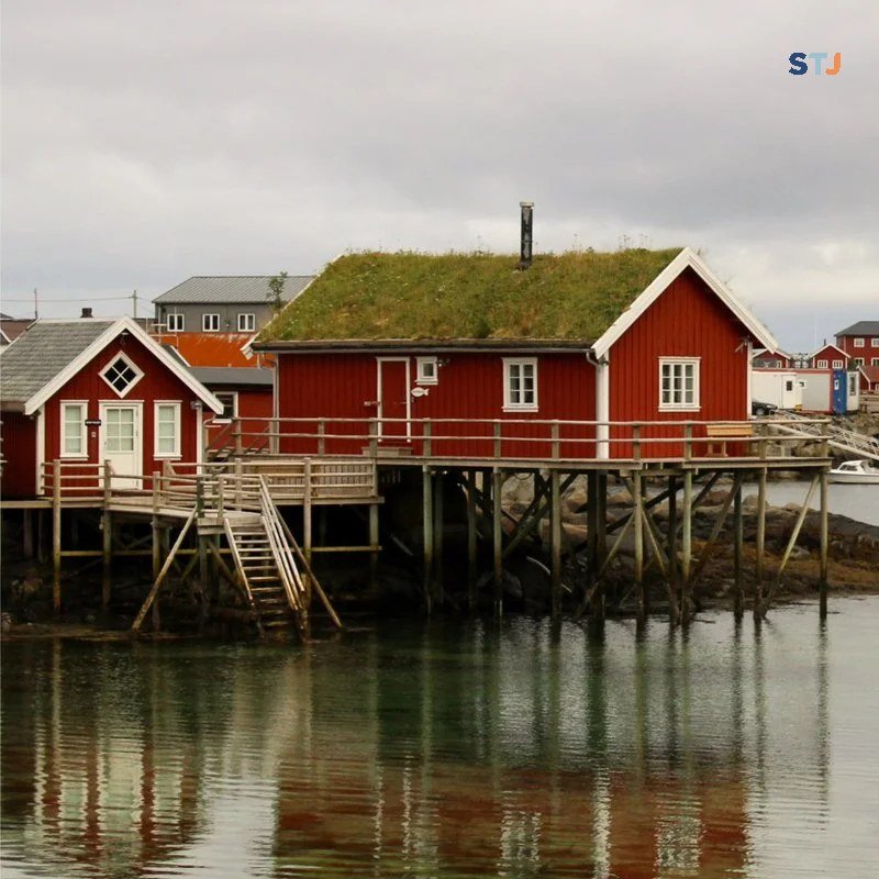 Red rorbu with a grass roof reflected in the water in Hamnøy, Lofoten