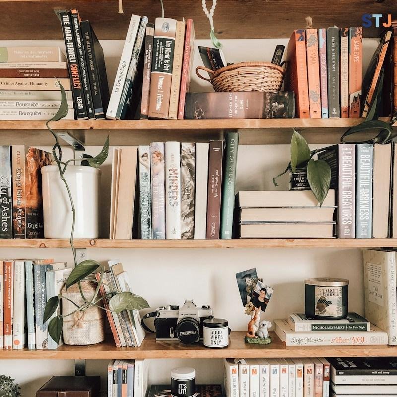 A stack of travel journalism and food books on a desk next to a camera.